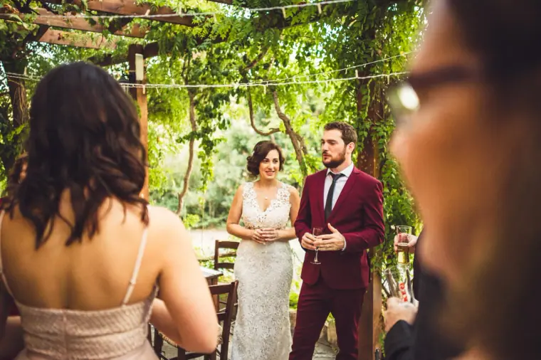 Newlyweds chatting with guests under the vine pergola, framed by guests in the foreground