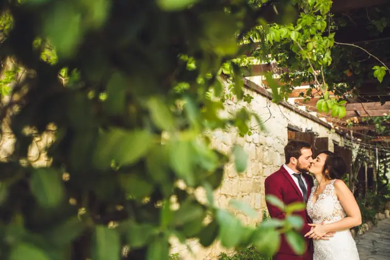 Couple kissing by the stone building, glimpsed through leafy branches