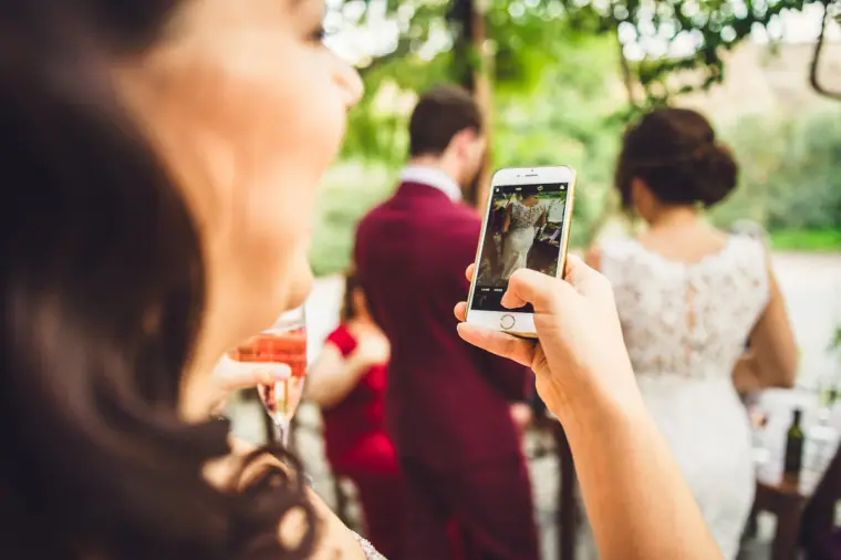 Guest photographing the newlyweds on her phone during the courtyard reception