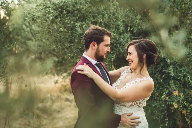 Bride laughing as she holds the groom in a shady olive grove