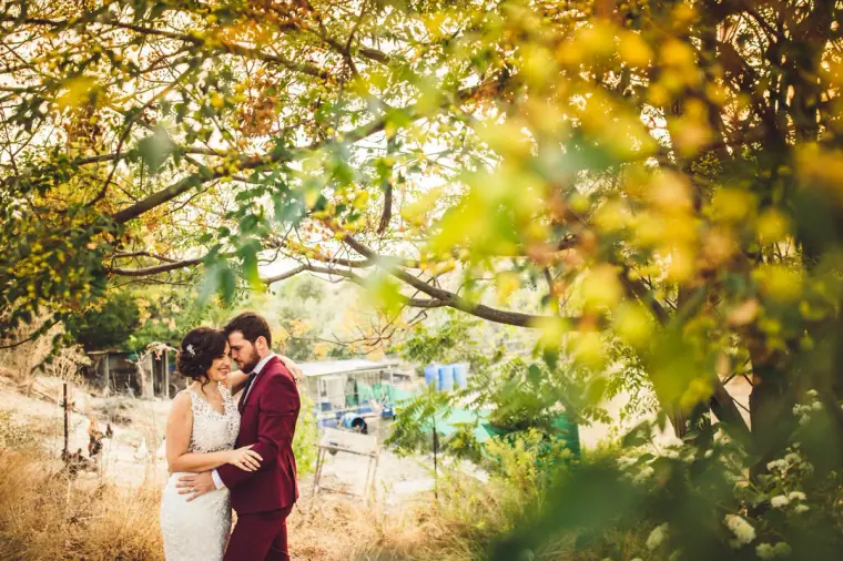 Bride and groom embracing under golden autumn branches, framed by leaves