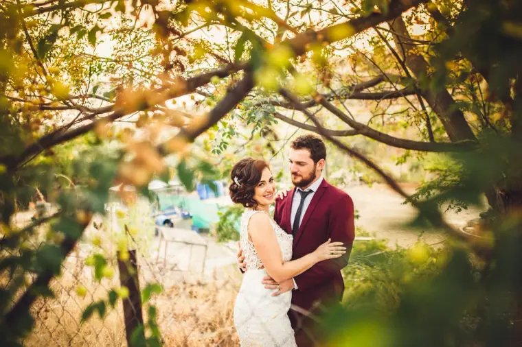 Newlyweds holding each other beneath overhanging branches at golden hour