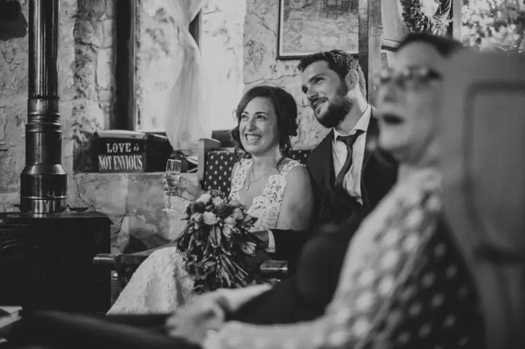Black-and-white photo of the bride laughing with her bouquet as the groom smiles beside her