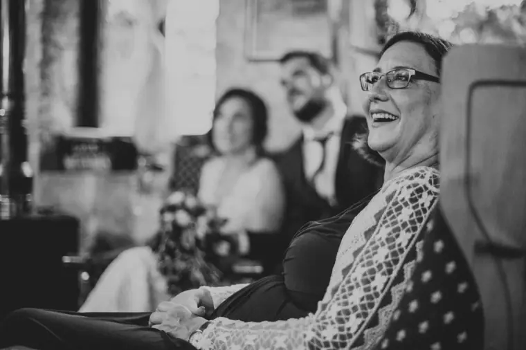 Black-and-white photo of a guest in glasses smiling with the newlyweds behind her