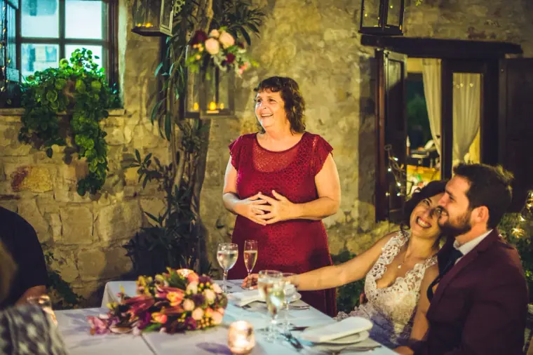 Guest in red giving a speech as the bride and groom laugh at the candlelit table