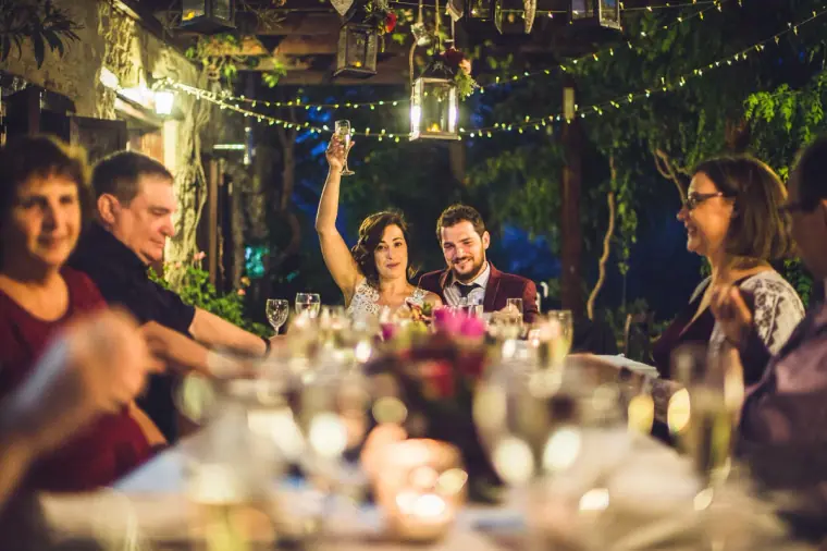 Bride raising her arm in celebration at the courtyard dinner under fairy lights