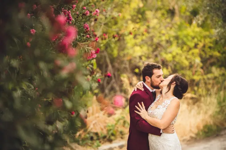 Madeliene and Itai kissing by pink oleanders, framed by soft foliage