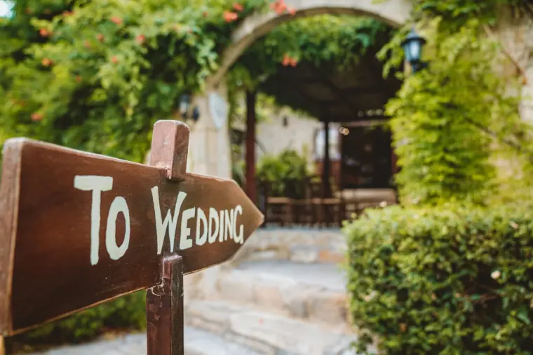 Hand-painted wooden "To Wedding" sign pointing towards the arched entrance of Vasilias Nikoklis Inn