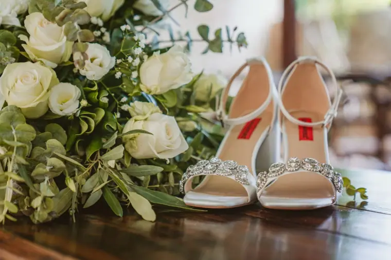 Sparkly bridal sandals beside a bouquet of white roses and eucalyptus
