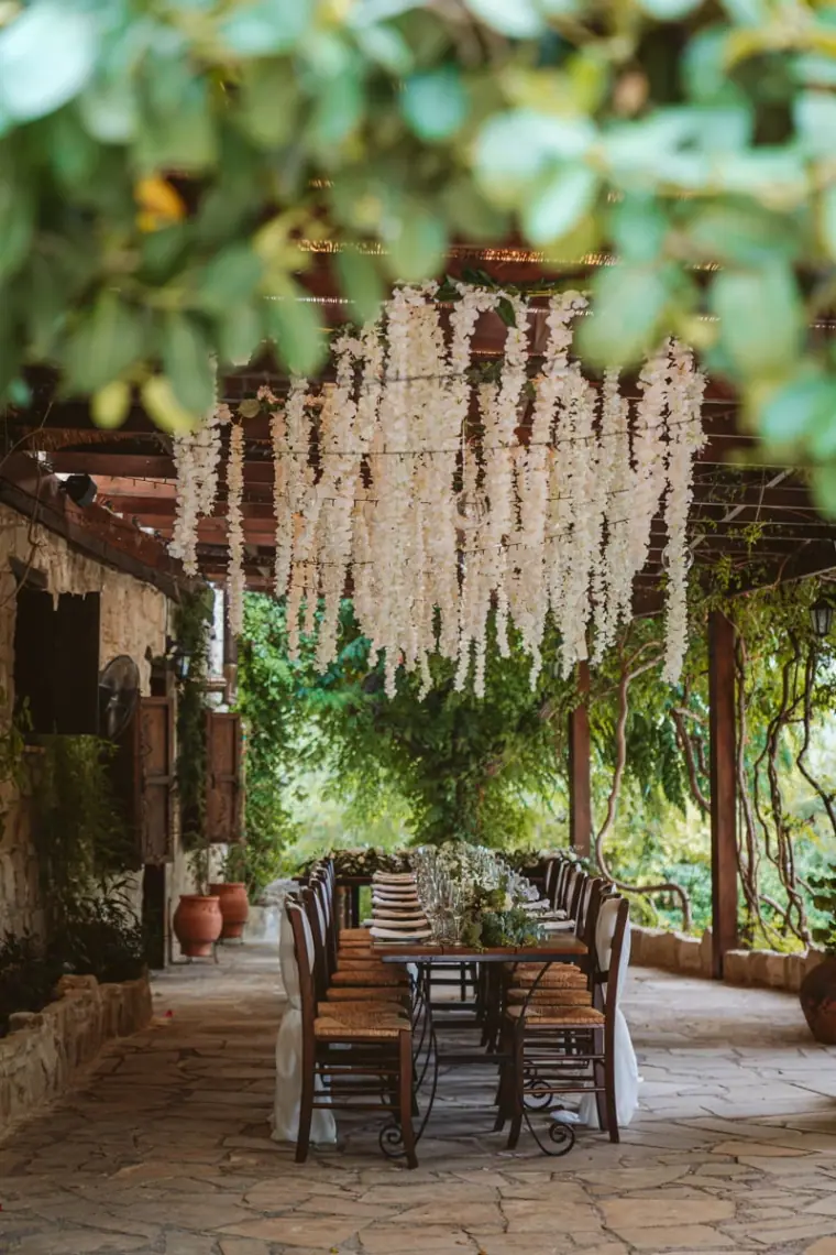 Courtyard dinner table beneath hanging white wisteria-style floral installation