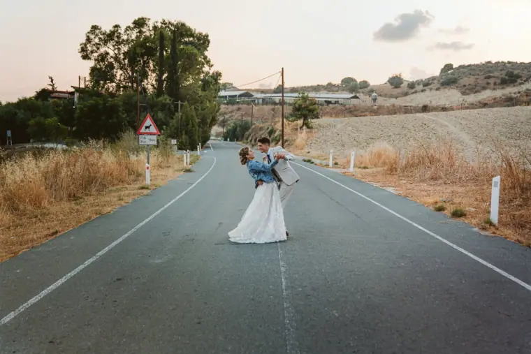 Groom dipping the bride in the middle of a quiet rural road at sunset