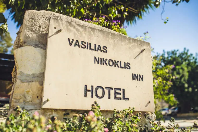 Carved stone sign for Vasilias Nikoklis Inn Hotel framed by greenery