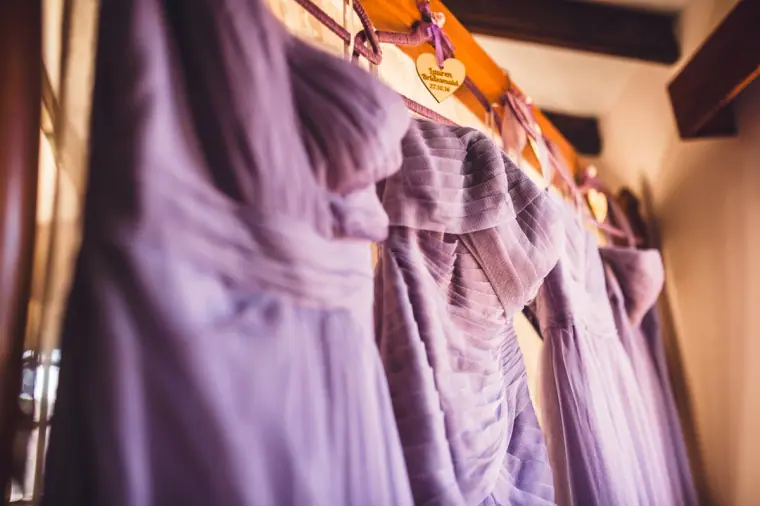 Lilac bridesmaid dresses hanging in a row on a wooden rail