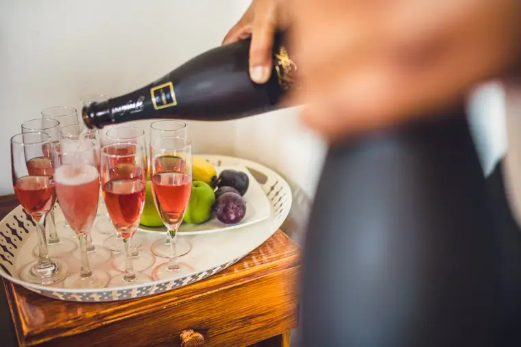 Sparkling rosé being poured into flutes beside a bowl of fruit