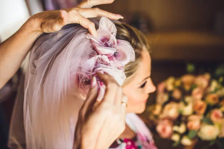Pink fabric flowers being pinned into the bride's hair beside her veil