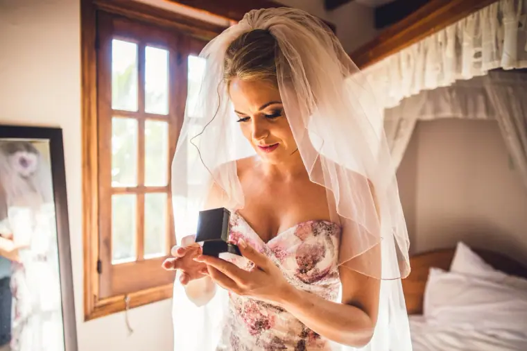 Bride in her veil opening a small ring box by the window
