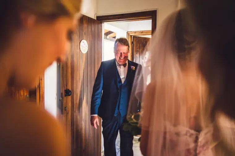 Older man in a navy suit stepping through the doorway to see the bride