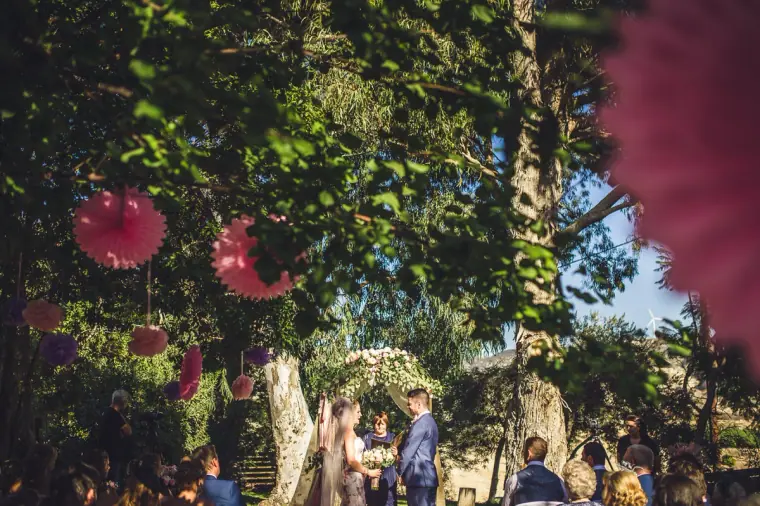 Wide view of the outdoor ceremony beneath trees hung with paper pompoms