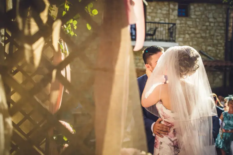 Bride and groom embracing after the ceremony, glimpsed past a wooden trellis