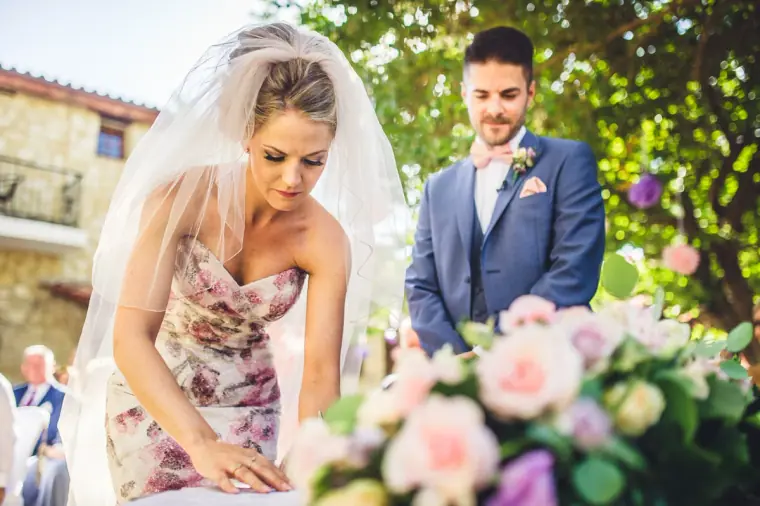 Bride in a floral gown signing the register beside a bouquet of pink roses