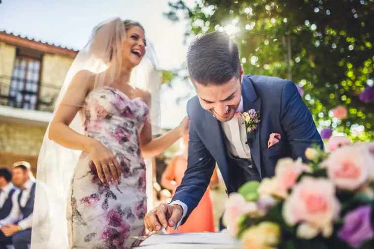 Groom laughing as he signs the register next to the bride