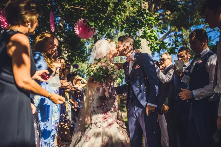 Newlyweds kissing as guests shower them with confetti in the garden