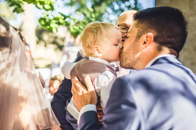 Groom kissing a toddler's cheek as guests congratulate the couple