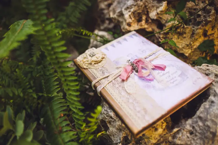 Lace-wrapped guest book tied with ribbon resting among ferns