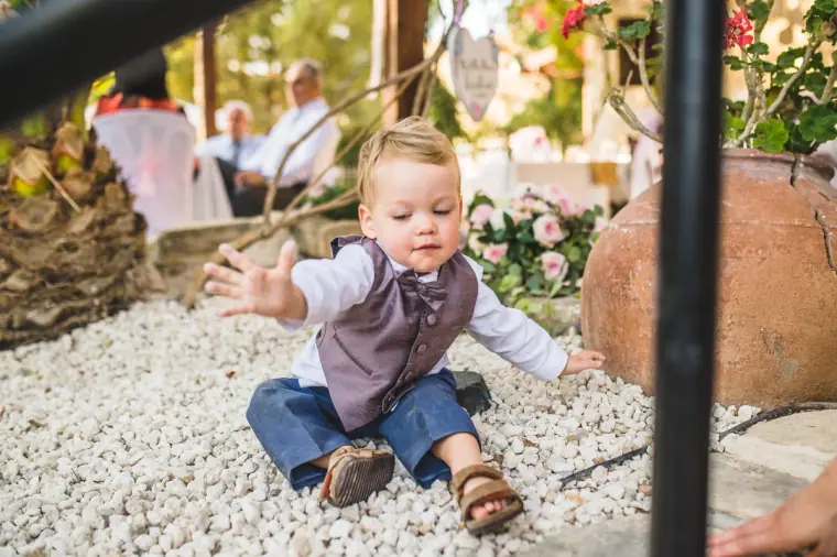Toddler in a waistcoat playing on white gravel at the reception