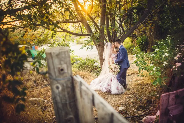 Couple standing together beyond a weathered wooden fence among trees