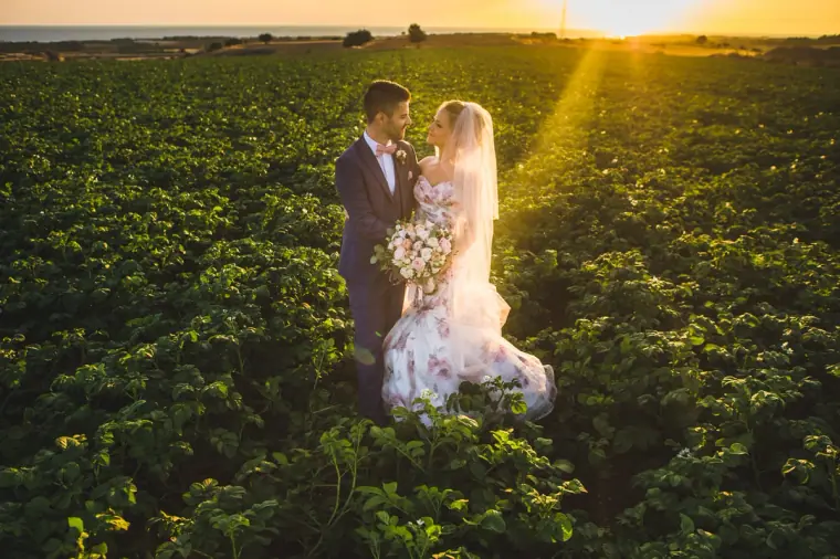 Bride and groom in a green field as the sun sets behind them