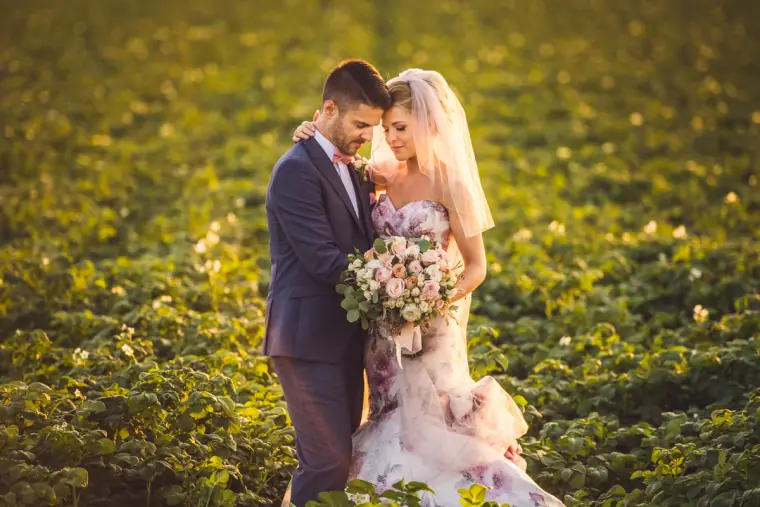 Bride and groom embracing in a leafy green field in evening light
