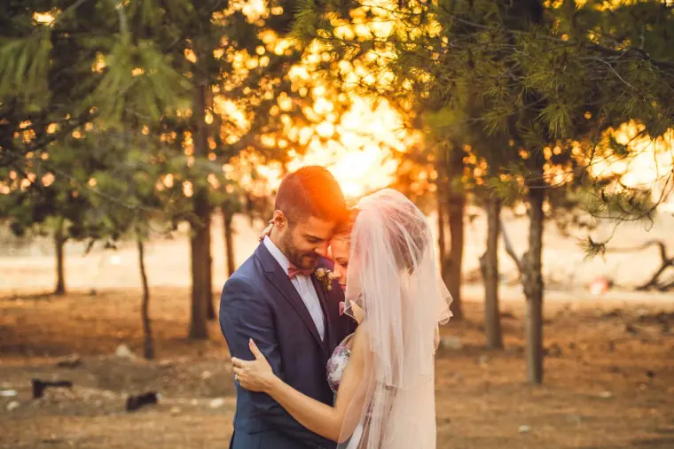 Couple touching foreheads as the sun sets through the trees behind them