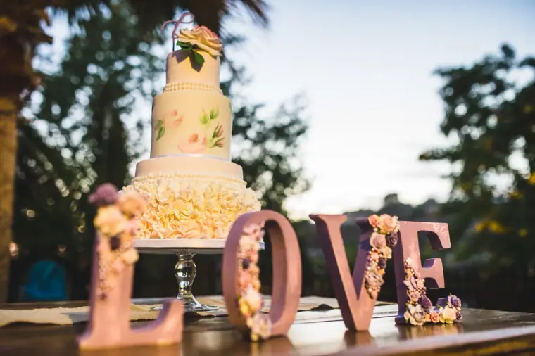 Tiered white wedding cake behind floral LOVE letters at dusk