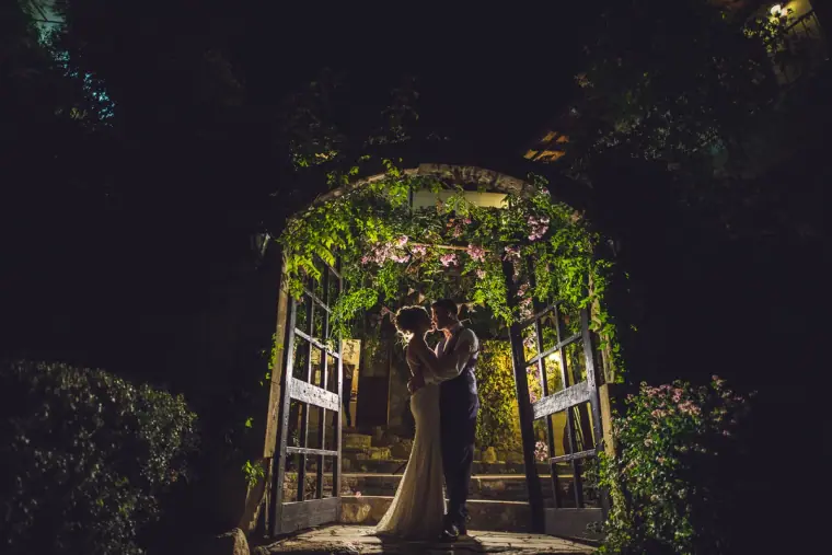 Couple kissing in the illuminated ivy-covered archway of Vasilias Nikoklis Inn at night