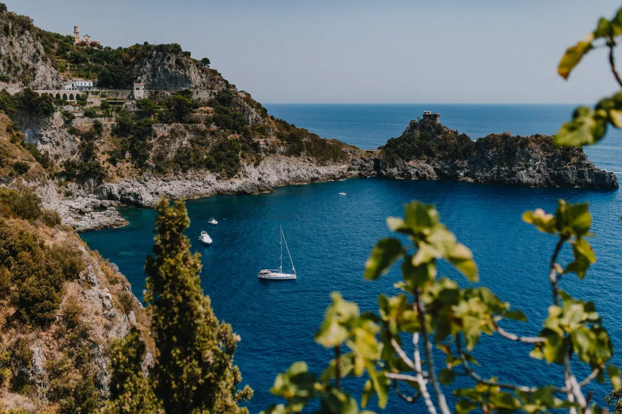 Turquoise bay with moored sailing boats below rugged cliffs on the Amalfi Coast, Italy