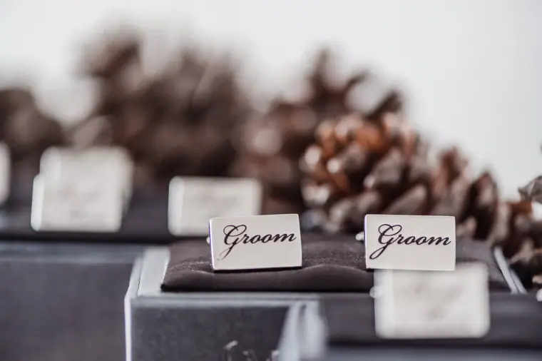 Engraved "Groom" boxes beside pine cones on a dark table