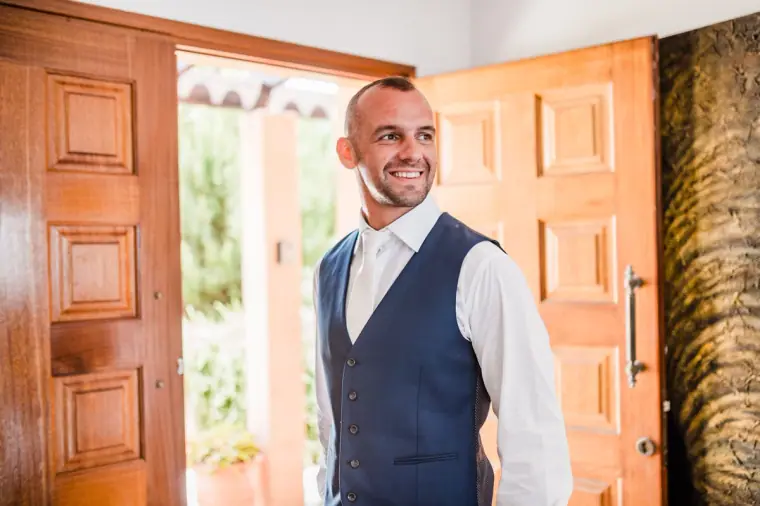 Groom in a navy waistcoat smiling in an open doorway