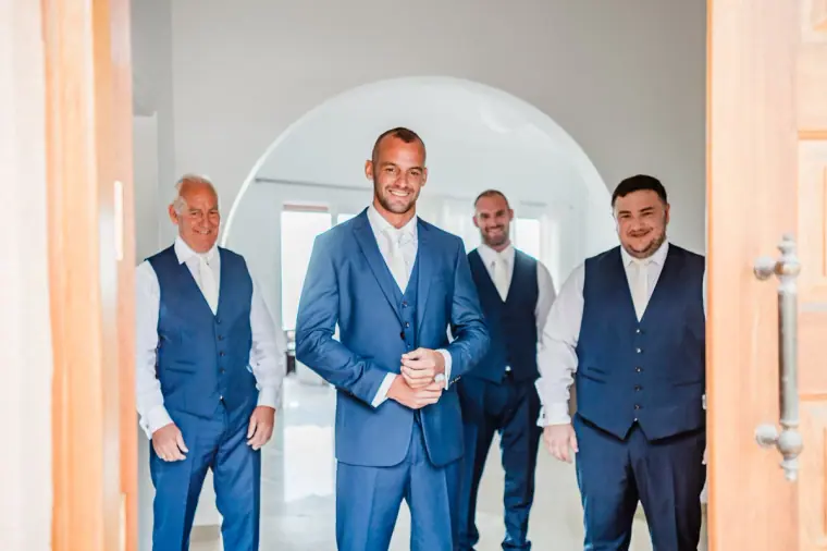 Groom and groomsmen in navy suits standing in a white arched hallway