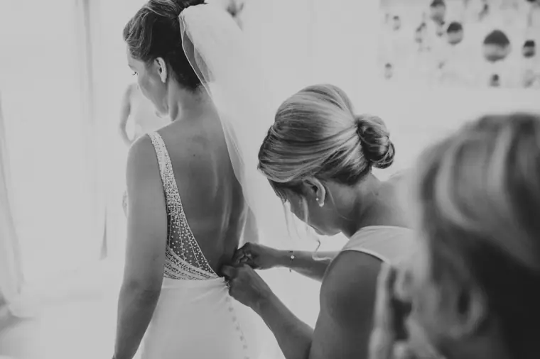 Black-and-white photo of a bridesmaid buttoning the bride's gown
