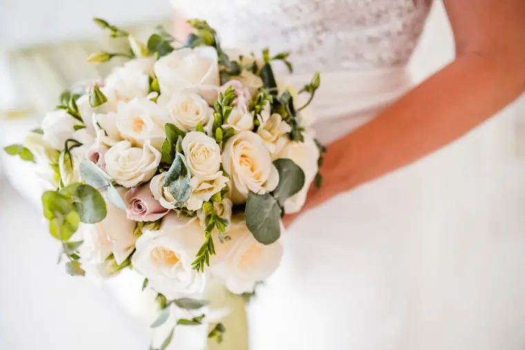 Close-up of the bride holding a bouquet of white and blush roses with eucalyptus