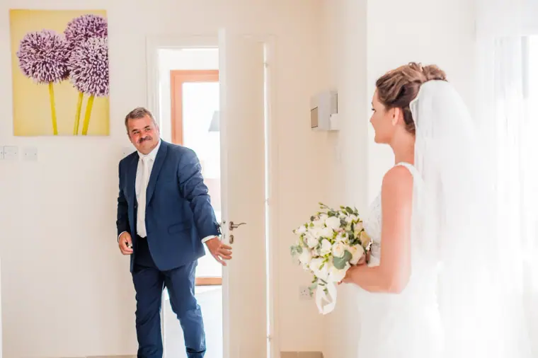 Older man in a navy suit stepping into the room to see the bride