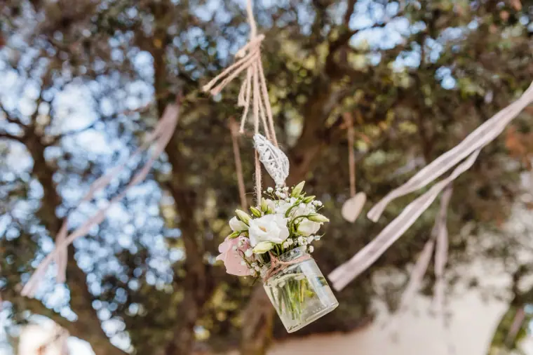Jar of white roses hanging from a tree on ribbons