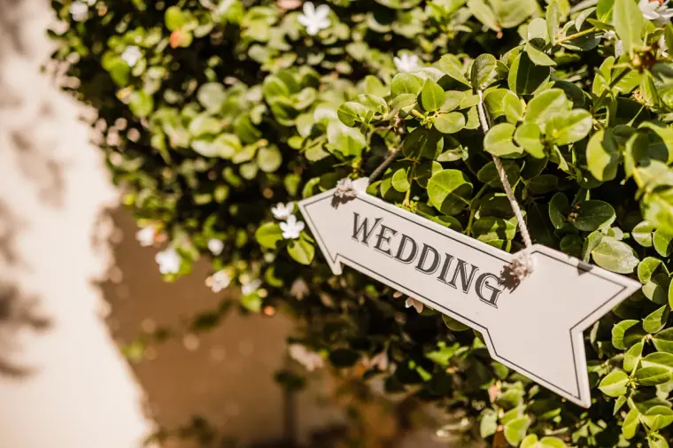 White wooden "Wedding" arrow sign hanging in the greenery