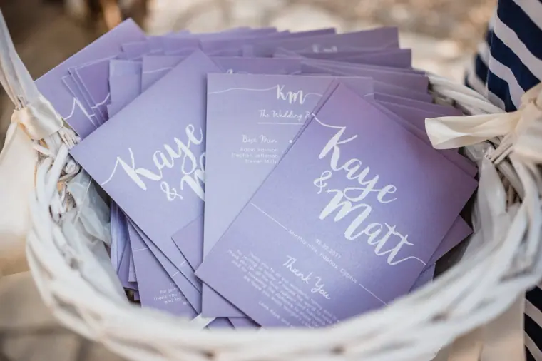 Lilac order-of-service cards for Kaye and Matt in a white wicker basket