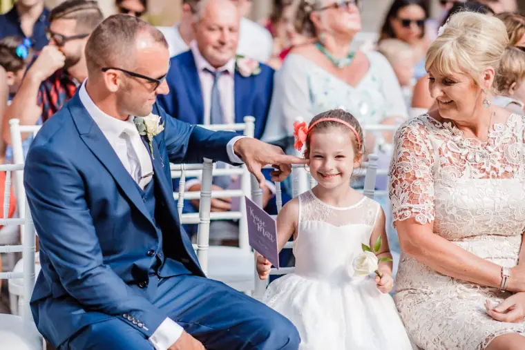 Guest in a navy suit chatting with a young girl in a white dress before the ceremony