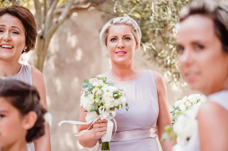 Bridesmaid in lilac holding a white rose bouquet as she waits to walk in