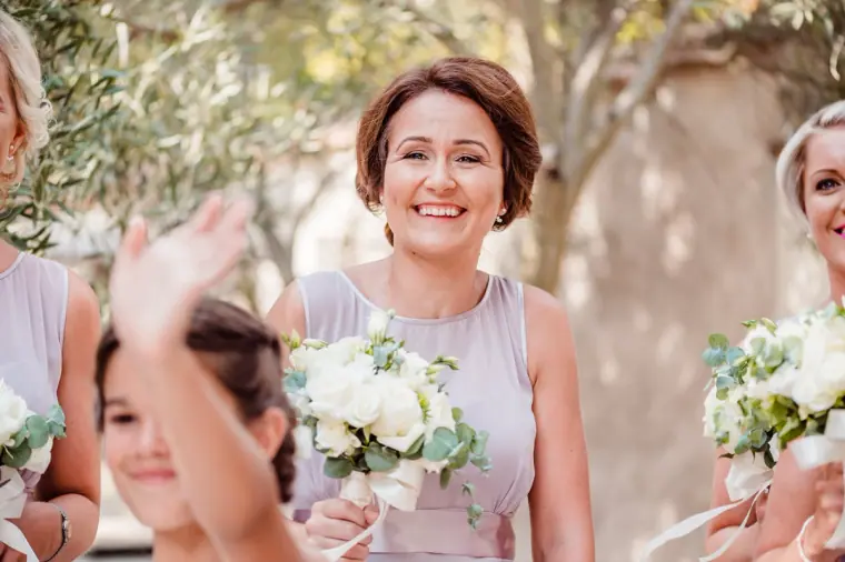 Smiling bridesmaid in lilac with her bouquet, a hand waving in the foreground
