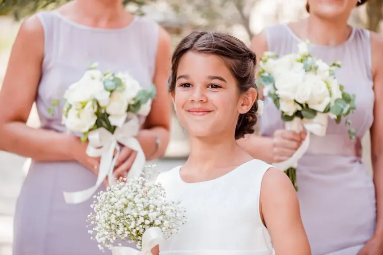 Flower girl in white smiling between bridesmaids in lilac