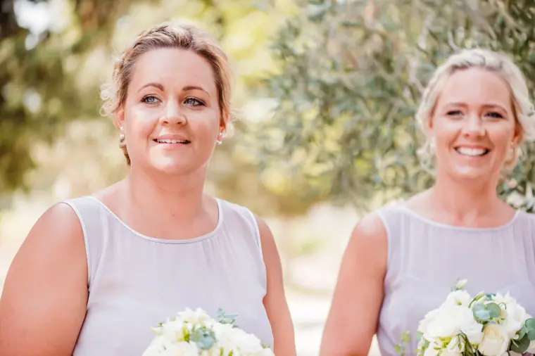 Two bridesmaids in lilac smiling with white rose bouquets